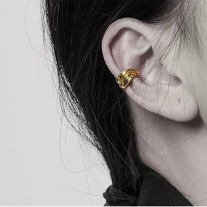 Minimalist gold wavy earcuff for non-pierced ears shown on model's ear in close-up