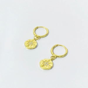 Détail macro de boucles d'oreilles créoles avec médaillons étoile et pierres blanches