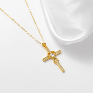 Detailed shot of a gold heart cross necklace with white zircon on a silk background