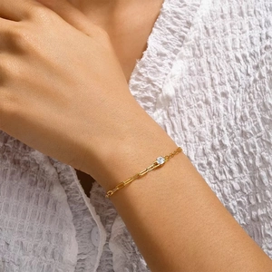 Detail of paperclip chain and white stone bracelet in gold finish on female wrist