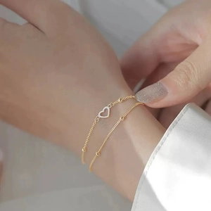 Close-up of double-layer gold chain bracelet featuring a hollow heart pendant and metal beads
