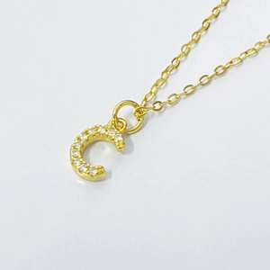 Close-up of golden letter C pendant inlaid with white zircons on a delicate chain