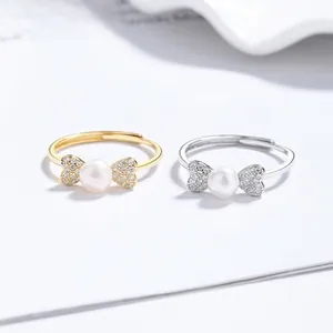Detail of adjustable silver and gold bow rings with center pearl and zircon accents