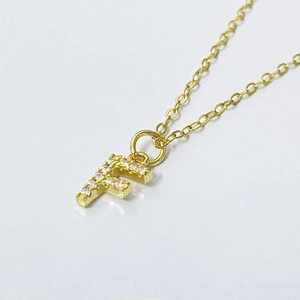 Macro view of gold letter F pendant with small zircon inlay on a delicate O-chain