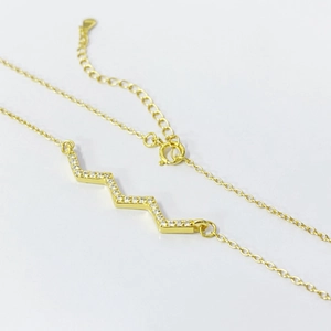 Close-up of gold wavy pendant necklace with sparkling cubic zirconia on white background