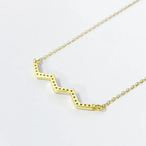 Detail of a gold zigzag pendant necklace with geometric patterns on a delicate chain