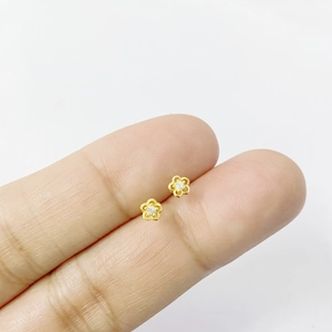 Gros plan de petites boucles d'oreilles fleurs dorées avec zircon entre les doigts