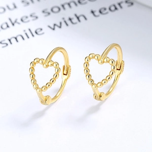 Macro shot of gold heart hoop earrings featuring a unique beaded texture and secure clasp