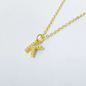 Macro detail of gold-plated K letter pendant necklace with micro-pave cubic zirconia crystals