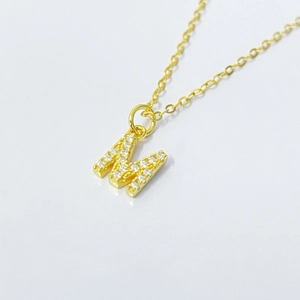 Detailed close-up of a gold M letter pendant with pavé-set shimmering zircon stones