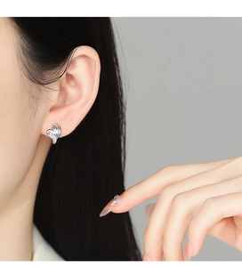 Close-up of 925 silver striped heart earring worn by a model in a minimalist studio setting