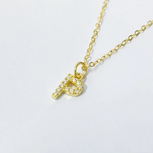 Close-up of golden letter P pendant with pavé cubic zirconia on a delicate chain