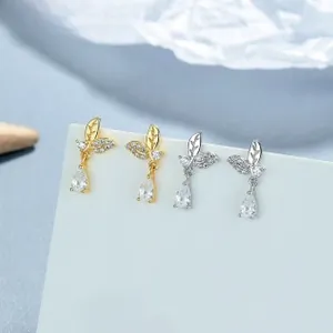Detailed view of gold and silver leaf earrings with teardrop zircon on display