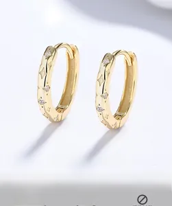 Close-up of gold hoop earrings with star engravings and inlaid cubic zirconia stones