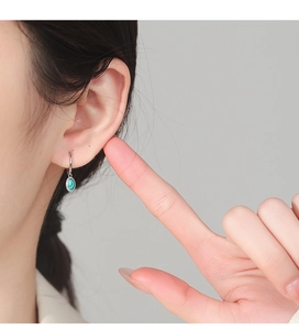 Detail showing a 925 silver hoop earring with green enamel pendant on a model