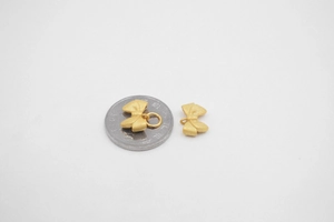 Macro view of matte gold bow pendants next to a coin for size reference comparison