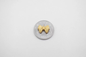 Macro detail of a matte gold bow pendant on a coin for size reference DIY jewelry