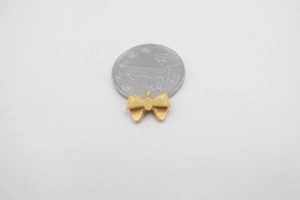 Detailed view of matte gold bow pendant size compared to a coin on flat background
