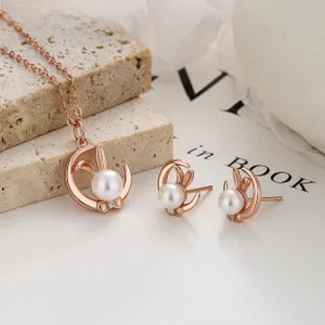Rose gold rabbit necklace and earrings set with white pearls on a stone background