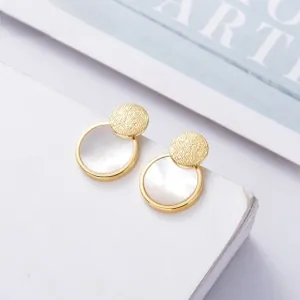 Detailed view of geometric shell earrings with gold metal and mother of pearl on a stand
