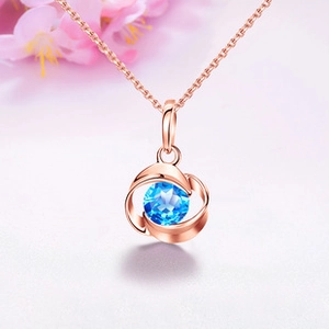 Macro shot of rose gold necklace featuring a faceted blue round stone in a curved frame