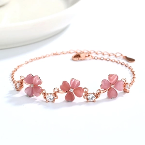 Close-up of rose gold four-leaf clover bracelet with pink opals and zircons on white surface