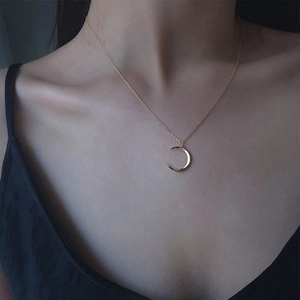 Detail of a minimalist gold crescent moon pendant on a delicate chain around the neckline