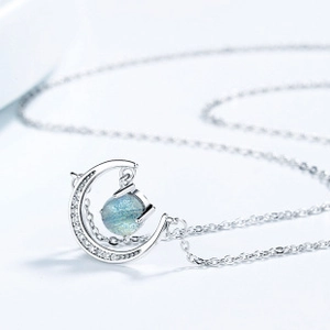 Macro shot of silver crescent moon pendant with micro-pave diamonds and blue gemstone