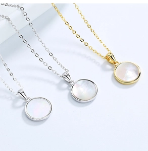 Détail de pendentifs ronds en nacre blanche sur d'élégantes chaînes en argent et or