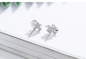 Macro view of polished silver four-leaf clover stud earrings on a white book edge