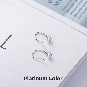 Close-up of white gold water drop silver earrings on a minimalist white magazine background