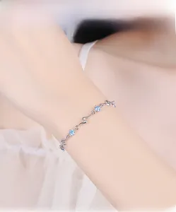Close-up of wavy silver bracelet with blue zircons worn on a female wrist with lace