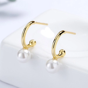 Macro view of gold minimalist C-shaped earring with elegant white pearl on ceramic stand
