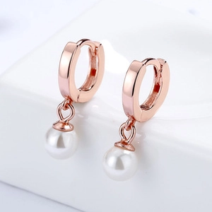 Macro detail of rose gold hoop earrings featuring elegant dangling white round pearls