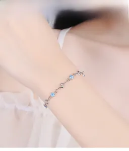 Detail of silver wavy link bracelet with blue zircon accents worn on female wrist