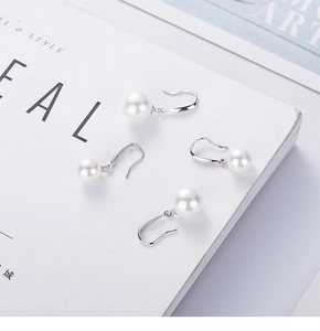 Detailed view of white round pearl earrings on S925 silver hooks on a fashion magazine