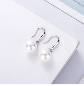 Macro detail of round white pearl earrings with minimalist silver hooks on white card