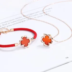 Detail of red clover pendant necklace and woven bracelet with rose gold plating