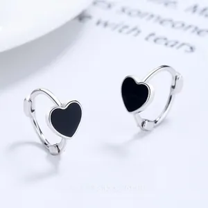 Detailed view of silver heart earrings with black enamel inlay on blue background