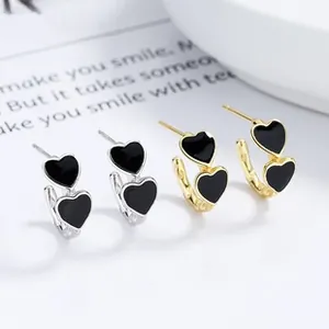 Close-up of heart-shaped drop earrings in gold and silver finish with black enamel