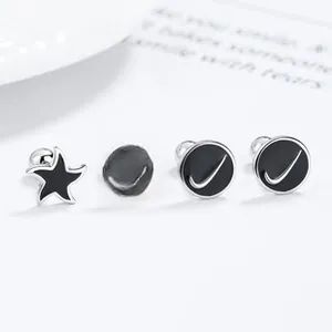Close-up of black enamel star and round silver stud earrings set on a white surface