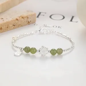 Macro shot of silver beaded bracelet with green jade-like beads and floral charm detail