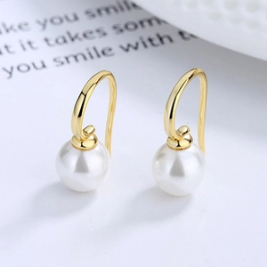 Macro shot of elegant round white pearl drop earrings with polished gold hooks