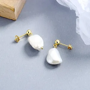Detail of baroque pearl stud earrings with golden fixings on a textured background