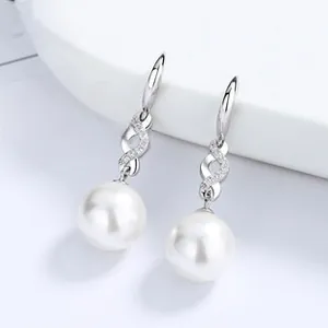 Gros plan de boucles d'oreilles perles avec courbes en métal argenté et zircons brillants