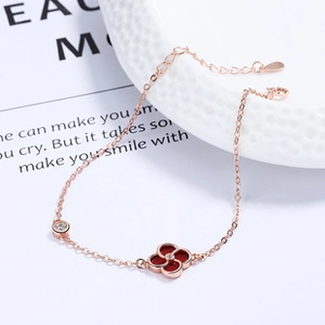Detail of rose gold clover bracelet with red enamel and small zircon on a white plate