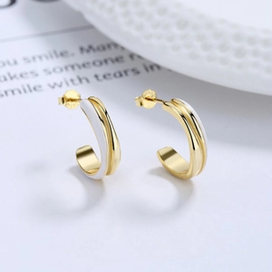 Gros plan détaillé des boucles d'oreilles dorées en C avec émail blanc et lisse