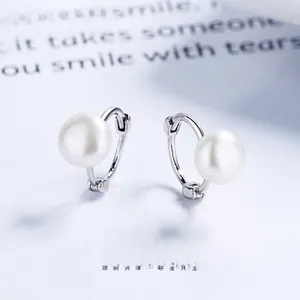 Detail of shell pearl earrings with silver metallic hoop on a vintage book background