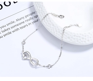 Detail of 925 silver infinity bracelet with small heart charms on a ceramic tray