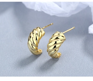 Close-up of golden croissant twist hoop earrings on a light blue textured background